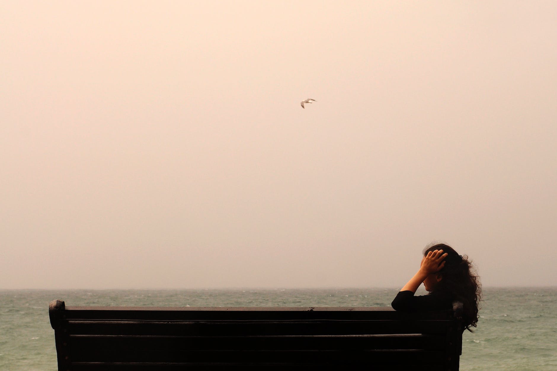anonymous woman sitting on bench near sea, grief and loss, grief, coping with grief, stages of grief, things that happen after grief, things that happen after losing someone